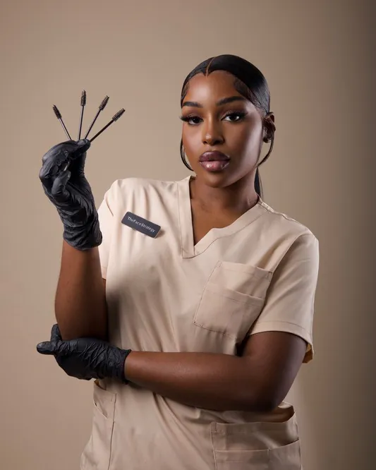 Nyasha, the artist behind The Face Strategy, in a beige uniform holding brow brushes